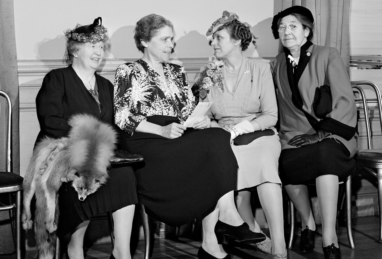 Four women in 1940s dress seated together in conversation, May 1945.